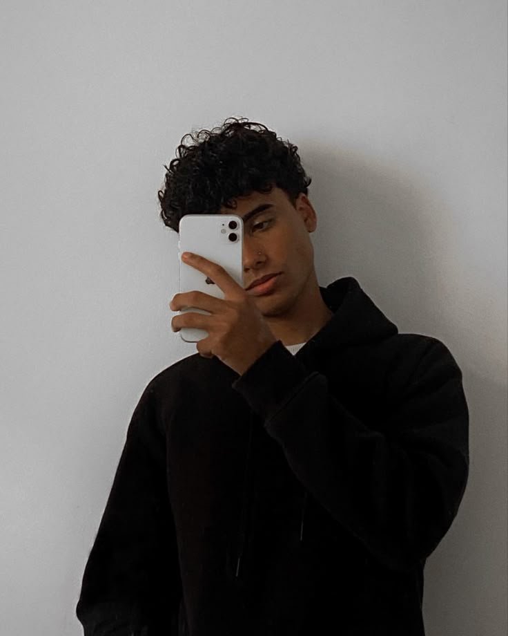 A young man in glasses writes in a notebook while sitting on a stylish couch indoors.